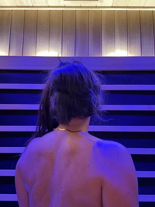 Woman relaxing inside the infrared sauna, back view with warm chromotherapy lighting